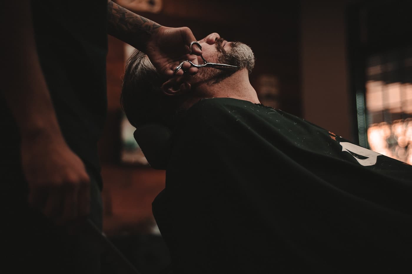 Barbeiro aparando a barba de um cliente na cadeira da barbearia