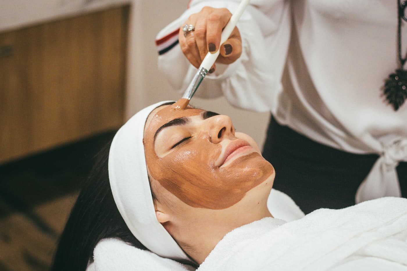 Esteticista aplicando máscara facial em uma cliente na maca